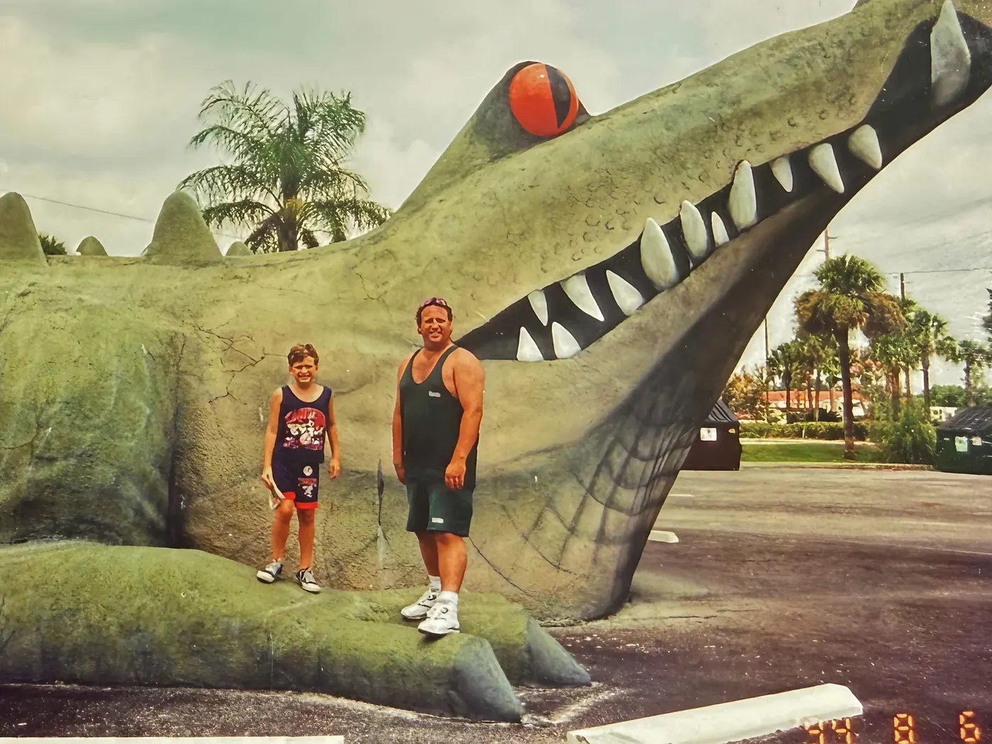 Erik as a kid standing with his dad in front of a giant alligator statue in Florida